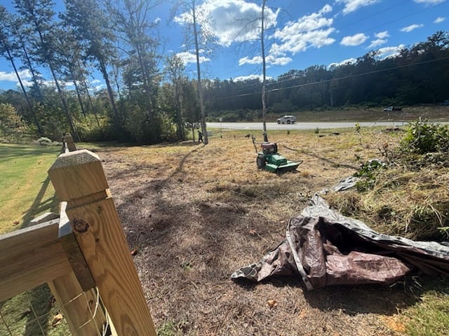 The same roadside lot cut down to the dirt, the brush mower parked in the middle and the cut growth tarped up for hauling