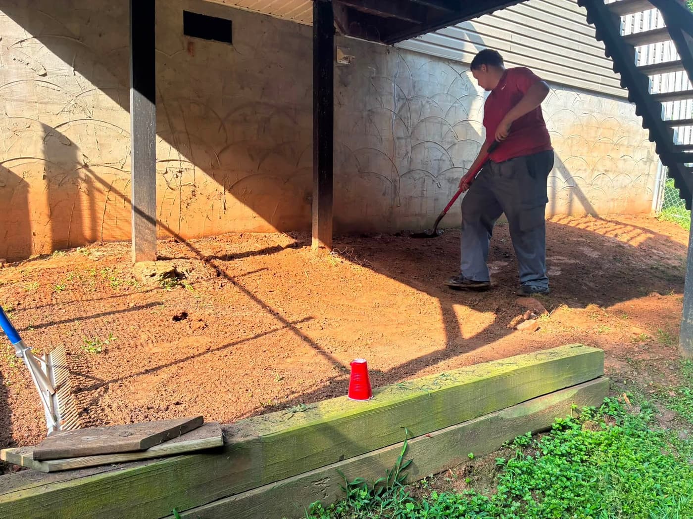 Kyler raking out ground under a deck on a landscaping job