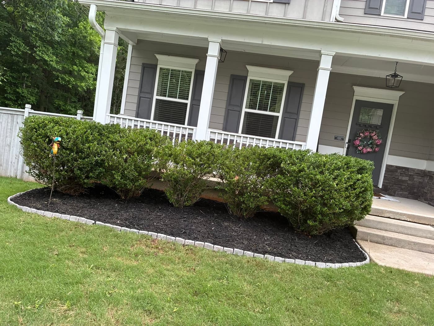 Fresh black mulch and stone edging along the front porch beds of a home in West Georgia, laid by Mason Worx
