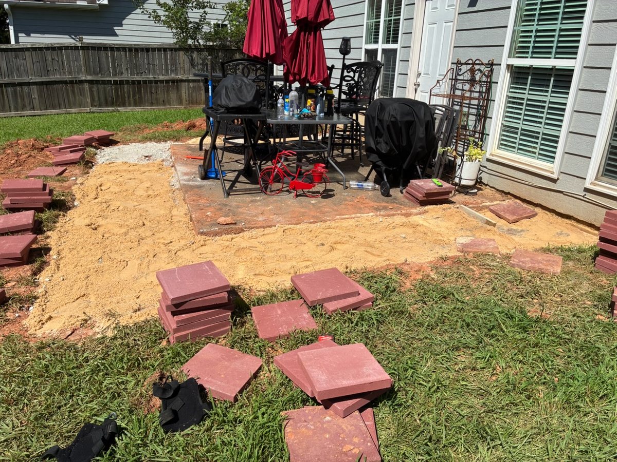 A backyard paver patio going in: sand base screeded flat, pavers stacked and ready