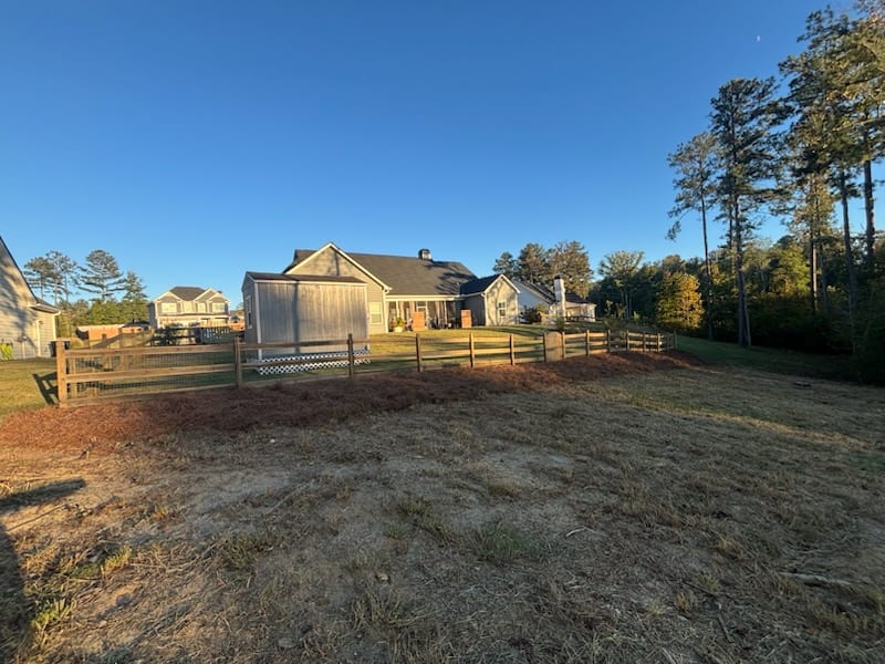 Fresh pine straw laid in long beds along a split rail fence line behind a house