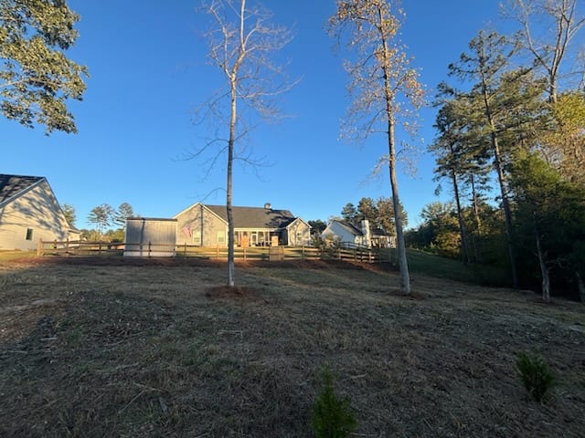 A back yard cleared and raked down to bare ground, young trees staked in and the house behind the fence line